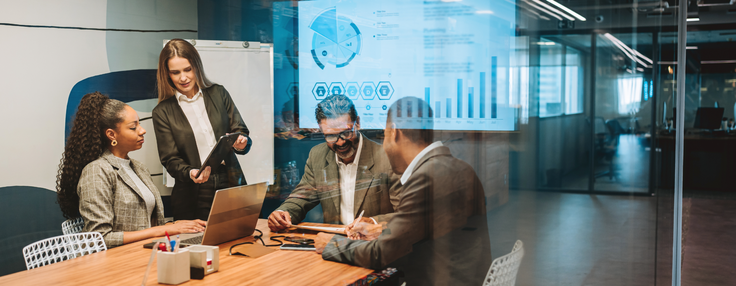 Team collaborating in a modern meeting room with digital dashboards in the background, illustrating how Open iT supports data-driven IT asset management.